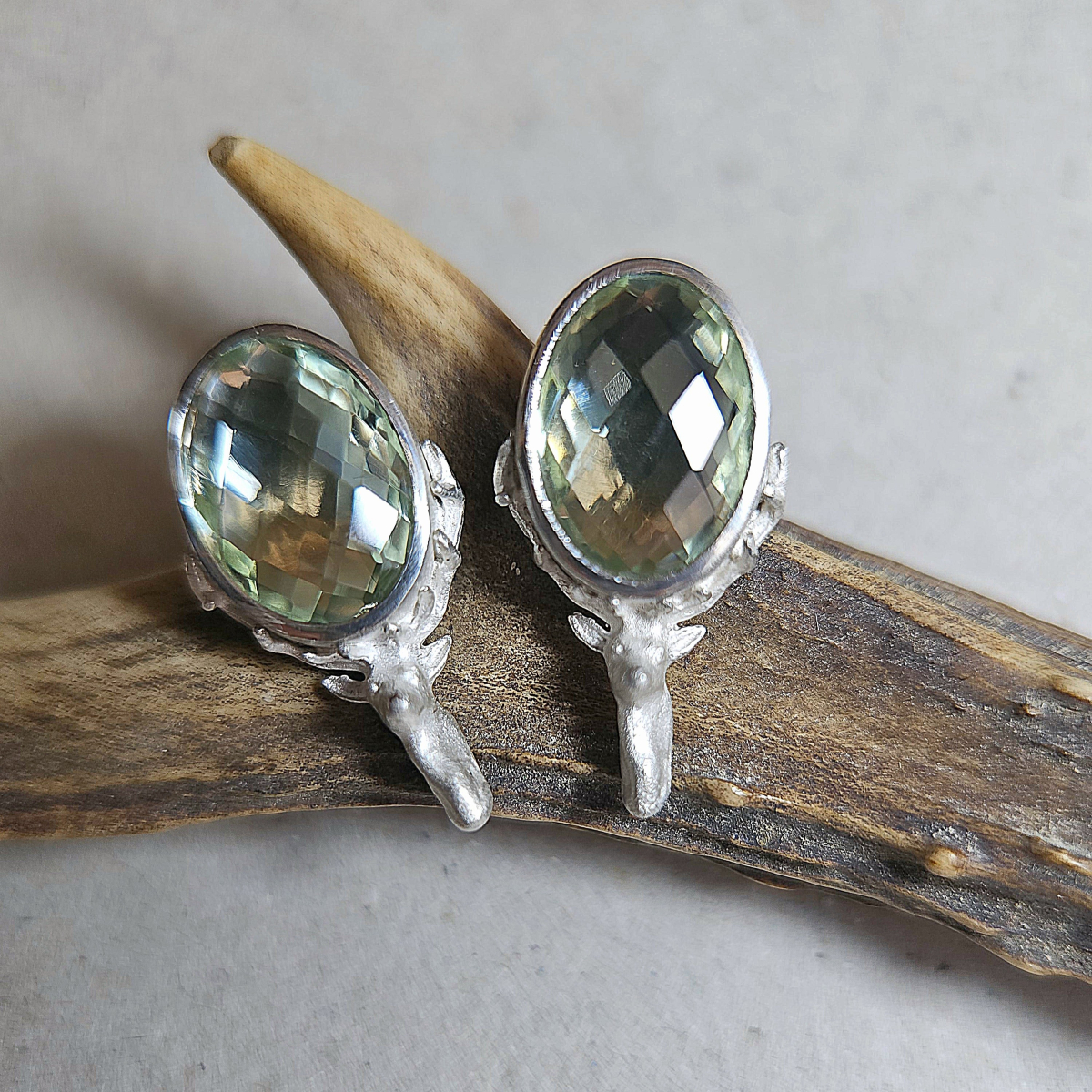 Preview: Ohrstecker mit Prasiolith und Hirschkopf aus 925 Silber auf einem Stück Rehgeweih