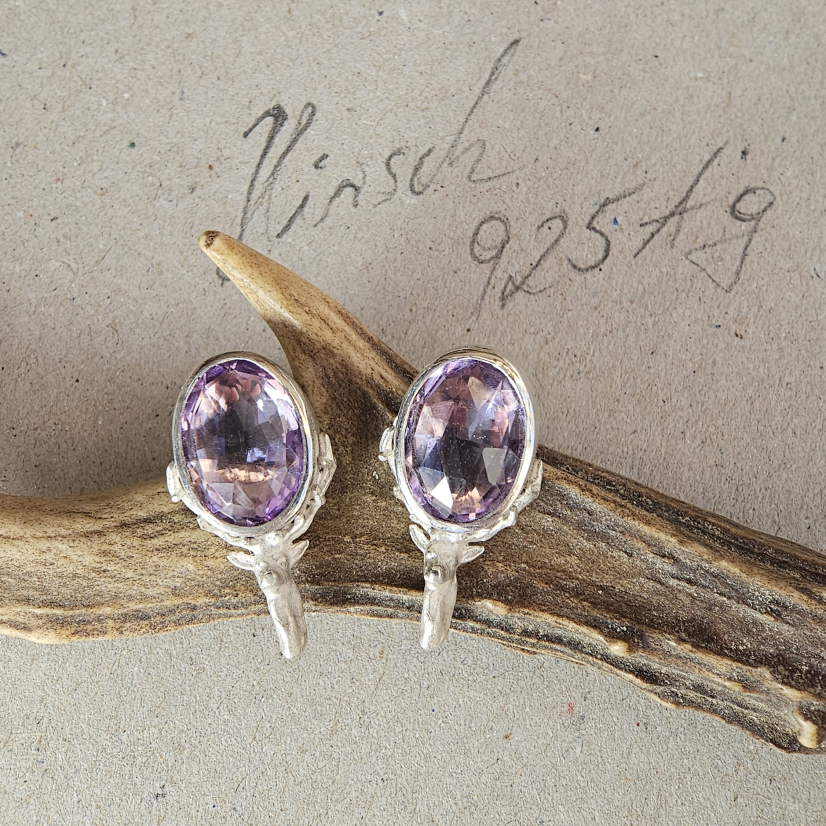 Preview: Ohrstecker mit Amethyst und Hirschmotiv aus 925 Silber auf einem Stück Rehgeweih